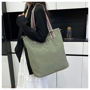 Detailed shot of large bean green tote bag with tricolor striped shoulder strap on a model