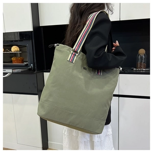 Olive green canvas tote bag detail featuring striped woven straps in lifestyle setting