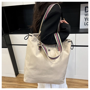 Detail view of a beige canvas bucket bag with red and blue striped strap and metal logo