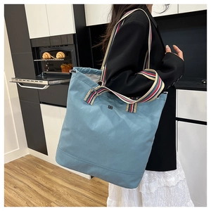 Close-up of grey-blue canvas tote bag featuring multi-colored striped shoulder straps