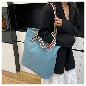Detail of light blue canvas tote bag featuring vibrant rainbow striped handles and drawstring