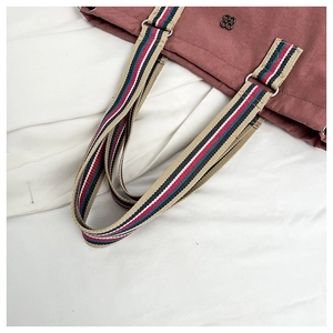 Detail of colorful striped woven strap and metal floral logo on dusty pink tote bag