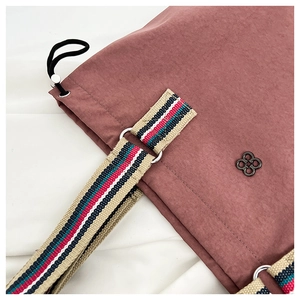 Detail of dusty rose nylon bucket bag featuring a colorful woven strap and clover logo