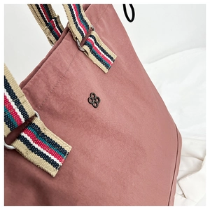 Detail of dusty pink tote bag showing pleated fabric texture and colorful striped handles