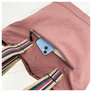 Detail of rose pink tote bag with striped straps showing a front zipper pocket for smartphone