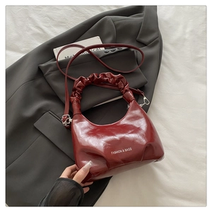 Detail of burgundy pleated handle and silver logo on a glossy semi-moon handbag