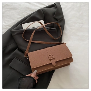 Detailed view of brown textured leather crossbody bag placed on a grey blazer suit