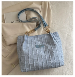 Detail of light blue tweed tote bag featuring textured grid fabric and gold metal buckles