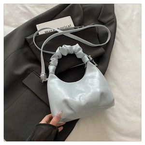 Detail of light blue pleated croissant bag on dark grey blazer with silver text