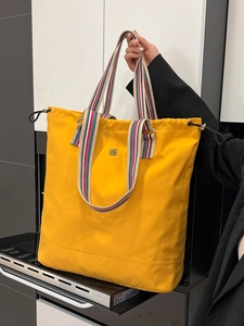 Bright yellow canvas tote bag with colorful striped handles and flower logo detail
