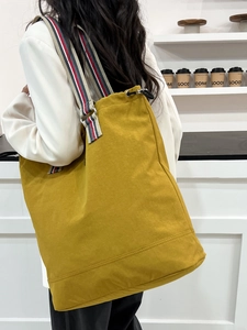Mustard yellow canvas tote bag with striped shoulder strap worn by a model in a cafe