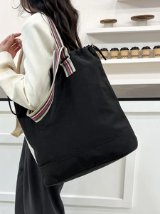 Large black canvas tote bag with striped shoulder strap worn by a model in a cafe