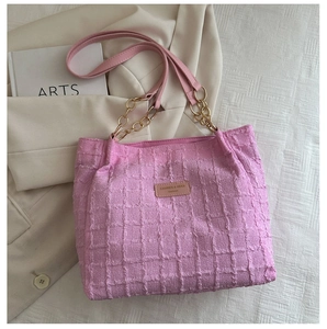 Detailed texture of pink woven tote bag with gold chain strap and leather logo tag