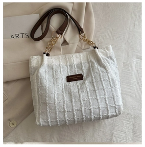 Detailed texture of white tweed tote bag with brown leather strap and gold chain
