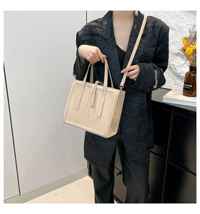 Close-up of beige minimalist tote bag with top handle and decorative straps on model
