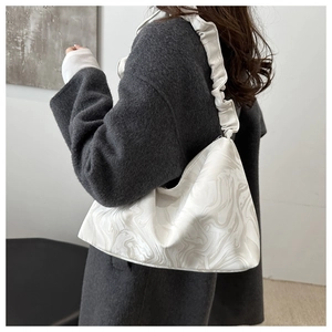 Détail d'un sac cabas à motif marbre blanc avec anse froncée porté sur un manteau gris