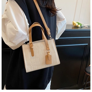 Detail of cream crocodile embossed handbag with brown handles and adjustable strap
