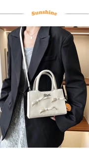 Détail du sac carré en cuir crème avec nœuds en perles et poignée en métal sous lumière douce