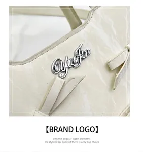 Détail du logo métallique YueJin argenté et du nœud sur le sac fourre-tout crème texturé