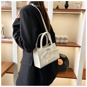 Détail d'un sac cabas blanc en cuir avec des nœuds perlés et un logo argenté brillant