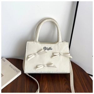 Détail du sac à main blanc crème avec trois nœuds et logo de marque métallique