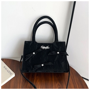 Détail du sac cabas noir avec texture gaufrée, nœuds décoratifs et perles blanches