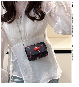 Close-up of black crossbody bag with cherry print and 3D cherry accent worn by model