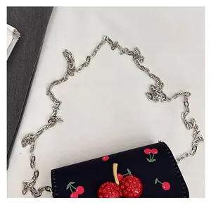 Detail of silver chain strap and cherry pattern on a black crossbody leather bag