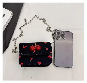 Mini cherry print crossbody bag size comparison next to a smartphone with silver chain
