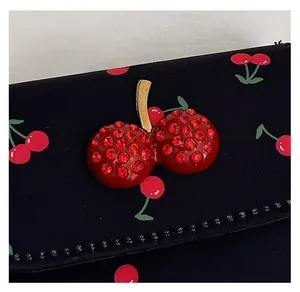Close-up of sparkling red rhinestone cherry charm on a black printed shoulder bag