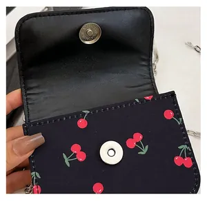 Detail of the magnetic buckle closure and cherry print on a black crossbody bag