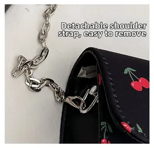 Detail of detachable silver chain strap on a black saddle bag with cherry print