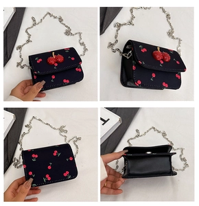 Detail view of mini black crossbody bag with red cherry prints and 3D cherry charm