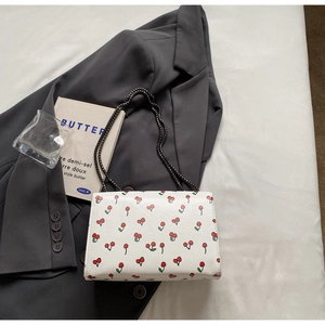 Détail d'un sac bandoulière blanc à motif cerise avec une fine bandoulière en chaîne métal