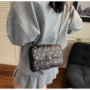 Détail d'un sac à bandoulière noir imprimé cerise avec chaîne et fermoir en métal