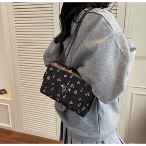 Détail du sac cerise avec fermoir à rivets emblématique et bandoulière chaîne grise