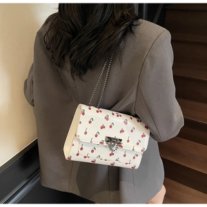 Detail of white cherry print crossbody bag featuring silver chain strap and metal lock