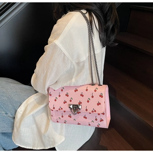 Pink cherry print shoulder bag with silver chain strap shown in a lifestyle setting