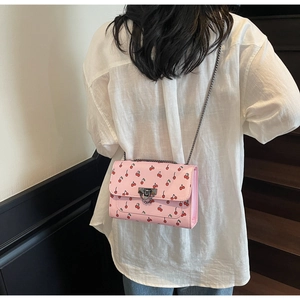 Détail du sac à bandoulière rose à motif cerise et chaîne en métal sur un mannequin