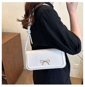 Détail d'un sac bandoulière blanc avec nœud doré porté sur un pull noir élégant