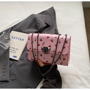 Détail d'un sac à bandoulière rose à motif cerises avec chaîne sur textile blanc
