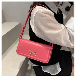 Détail d'un sac bandoulière rose avec fermoir noeud doré sur fond minimaliste
