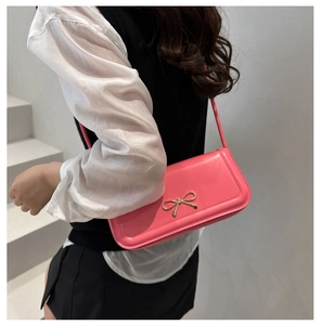 Seitenansicht einer pinkfarbenen Lederhandtasche mit goldener Schleife als Umhängetasche