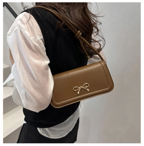 Détail d'un sac porté épaule en cuir marron avec un nœud doré porté par un mannequin