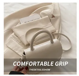 Detail of minimalist cream leather handbag with cylindrical top handle and crossbody strap