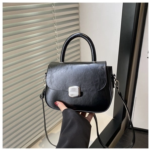 Detail of black glossy textured handbag featuring silver buckle and round handle
