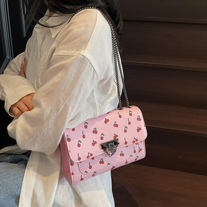 Sac bandoulière rose avec imprimé cerise et chaîne en métal porté par un mannequin