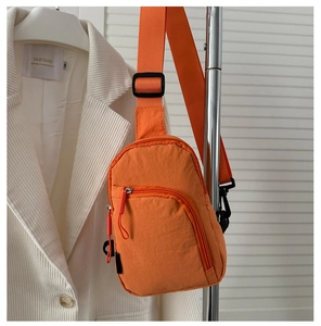 Détail d'un sac de poitrine en nylon orange vif avec sangles noires réglables et fermetures