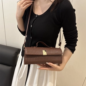 Brown woven rectangular crossbody bag with gold buckle on shoulder of model