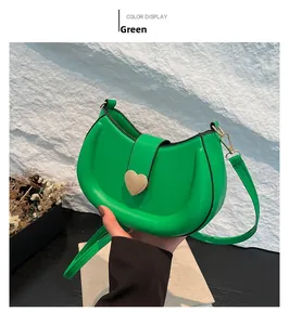 Close-up of green leather saddle bag featuring a gold heart buckle and fine shoulder strap